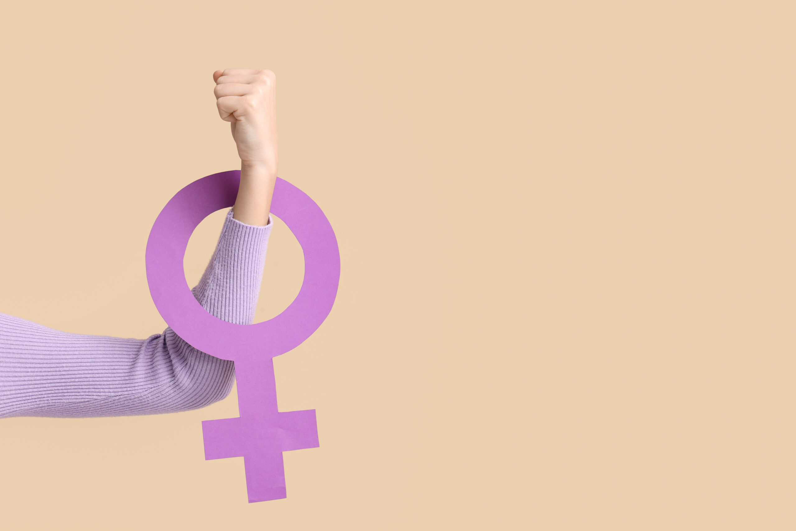 Young woman with female symbol showing muscles on beige background. Women’s history month